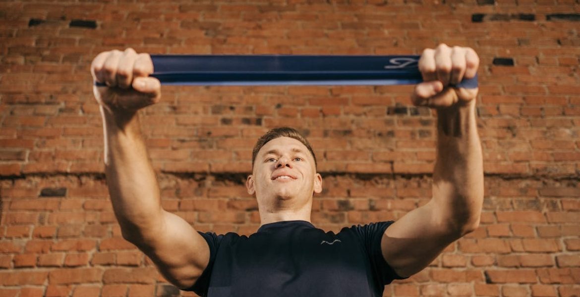 Man performing workout with resistance band against a brick wall backdrop.