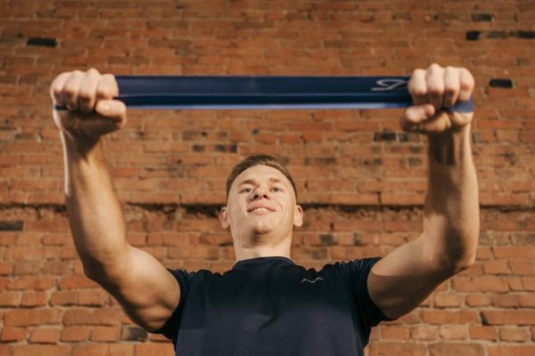 Man performing workout with resistance band against a brick wall backdrop.